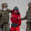 Soldados del ejército conducen a un joven en la playa ceutí de El Tarajal, hoy miércoles durante la masiva entrada de migrantes por la frontera que une la ciudad autónoma con Marruecos. 