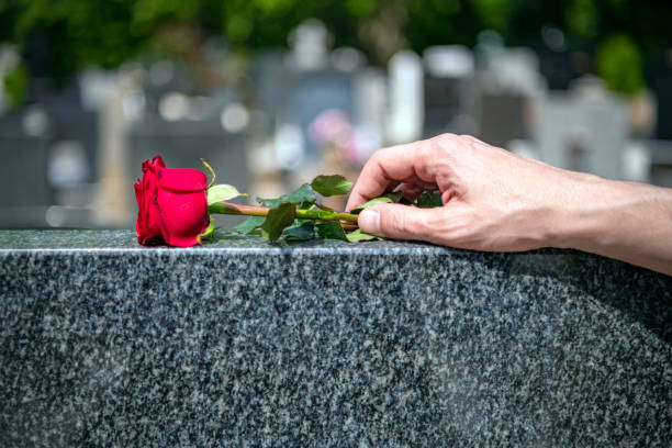 Una mano deposita una rosa en una tumba de un cementerio