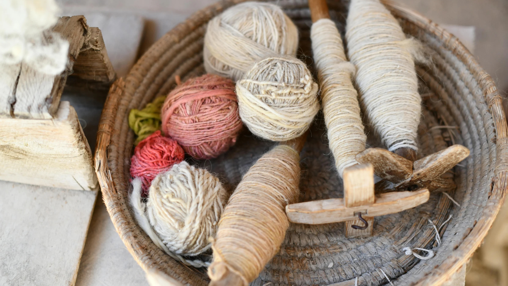 Madejas de lana e instrumentos tradicionales de hilado dispuestos en una cesta artesanal.