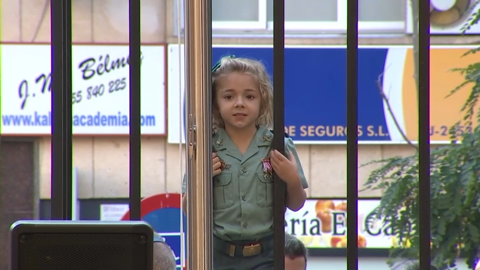 una niña contempla el desfile desde la reja