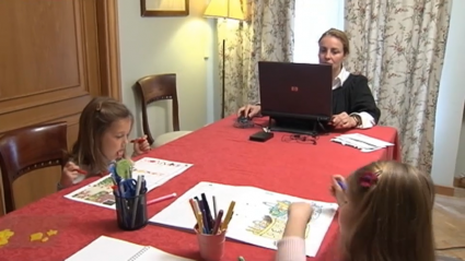 Una mujer trabaja desde su casa en una mesa junto a dos niñas
