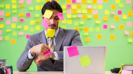 Salud laboral. Trabajador con infinitas tareas lleno de post-it.