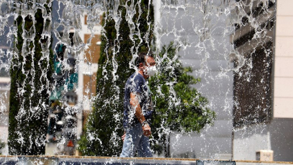 un hombre pasea con mascarilla cerca de una fuente