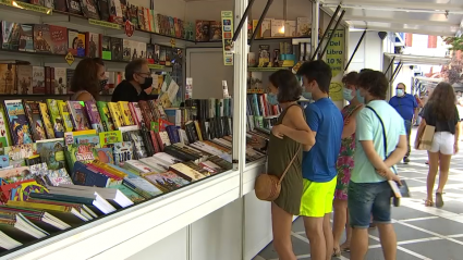 Varias personas viendo libros en una caseta de la feria del libro