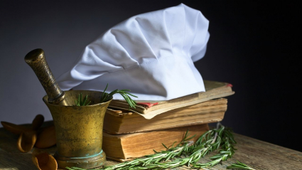 Elementos propios de la cocina. Mortero, gorro de chef, libros antiguos y hierbas