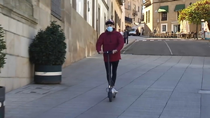 Un joven circula con un patinete eléctrico por una vía urbana