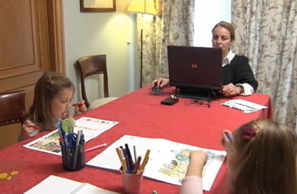 Una mujer trabaja desde su casa en una mesa junto a dos niñas